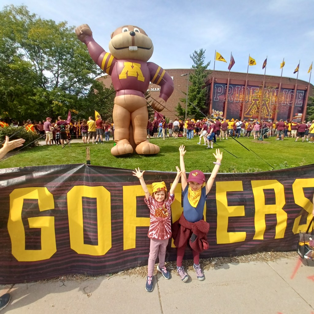 Two kids standing in front of inflatable mascot at a football game