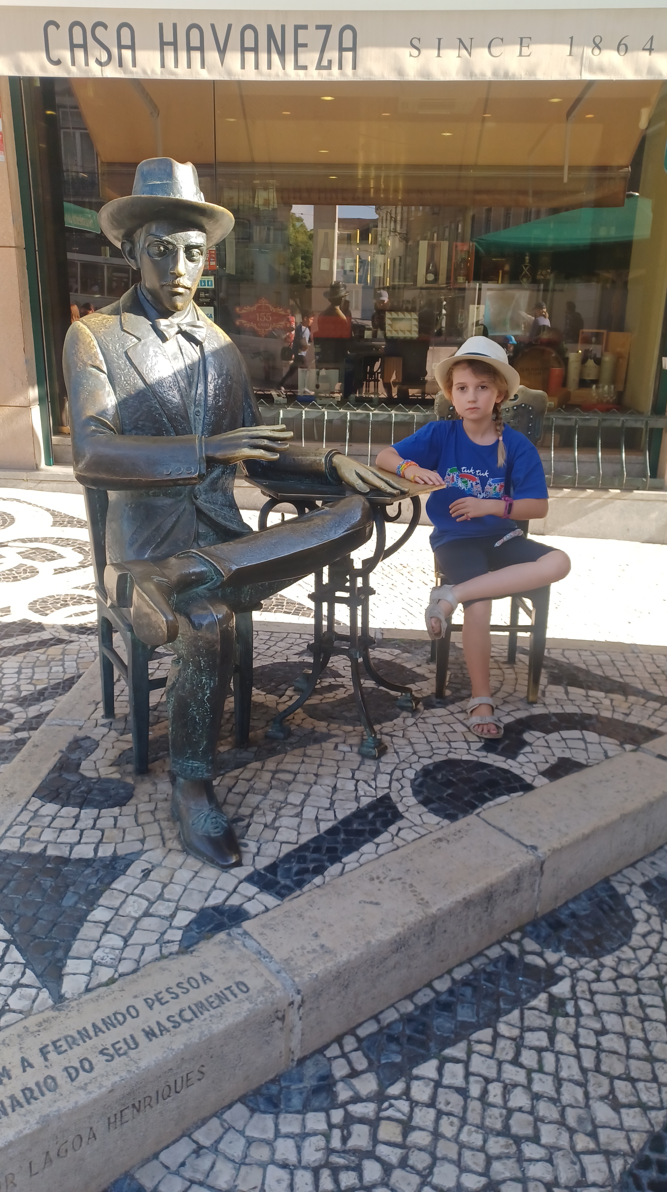 Young girl mimicking pose of large bronze statue while sitting down